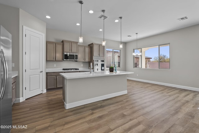 kitchen with decorative light fixtures, hardwood / wood-style flooring, a notable chandelier, an island with sink, and stainless steel appliances