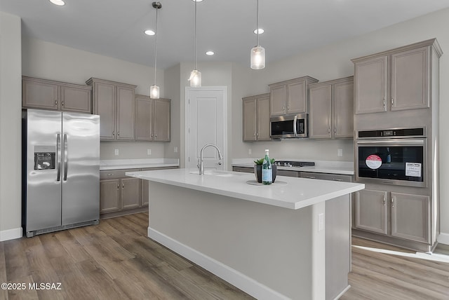 kitchen featuring wood-type flooring, a kitchen island with sink, sink, decorative light fixtures, and stainless steel appliances