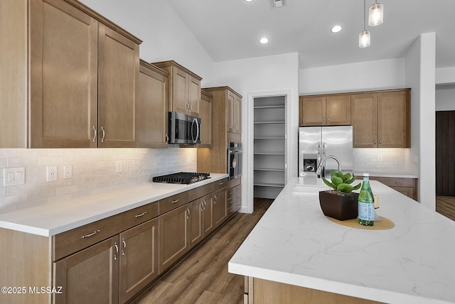 kitchen featuring decorative light fixtures, backsplash, a kitchen island with sink, and appliances with stainless steel finishes