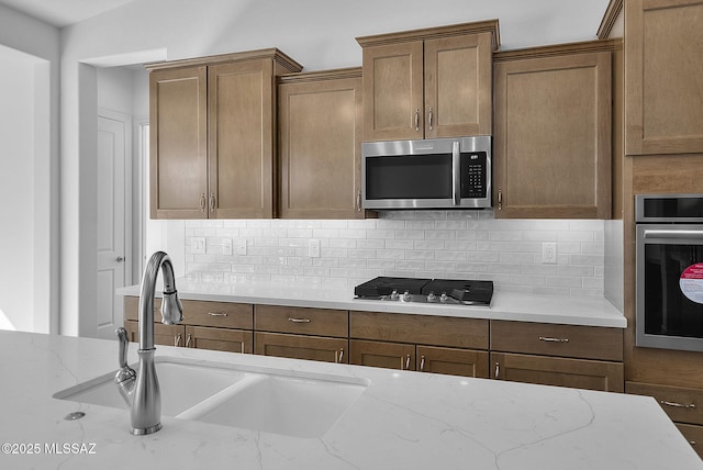 kitchen featuring sink, backsplash, light stone countertops, and stainless steel appliances