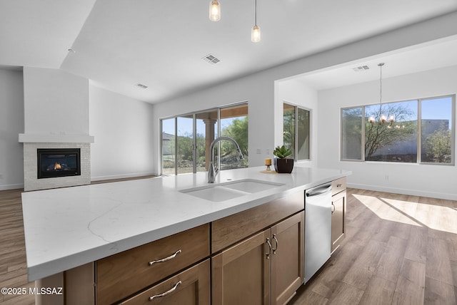 kitchen featuring pendant lighting, dishwasher, light hardwood / wood-style floors, sink, and light stone counters