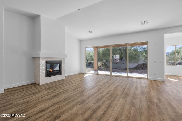 unfurnished living room with wood-type flooring, a brick fireplace, a healthy amount of sunlight, and lofted ceiling