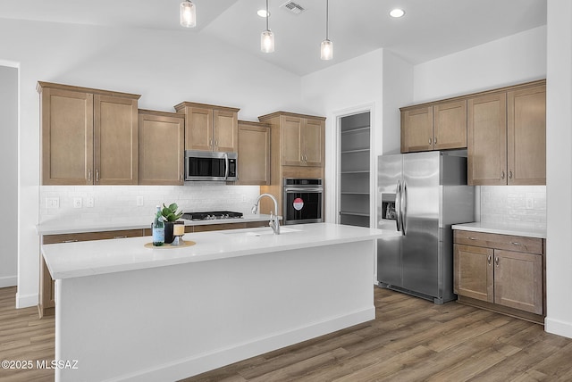 kitchen with appliances with stainless steel finishes, an island with sink, decorative backsplash, sink, and hanging light fixtures
