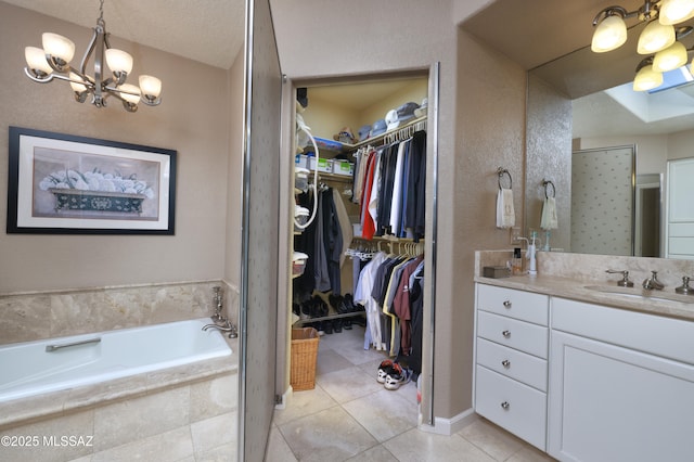 bathroom with tiled bath, vanity, tile patterned floors, a textured ceiling, and a chandelier