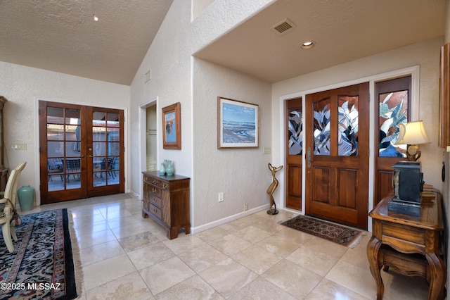 foyer with a textured ceiling, vaulted ceiling, french doors, and light tile patterned flooring