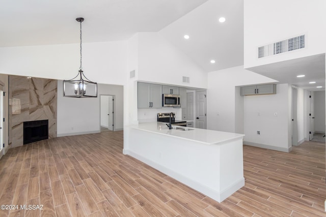 kitchen featuring gray cabinets, kitchen peninsula, stainless steel appliances, high vaulted ceiling, and a high end fireplace