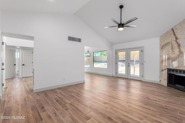 unfurnished living room with ceiling fan with notable chandelier, french doors, a large fireplace, light wood-type flooring, and high vaulted ceiling