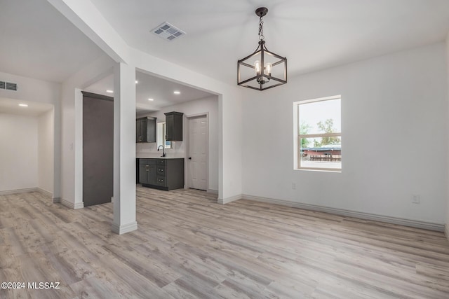 unfurnished dining area featuring sink, a chandelier, and light wood-type flooring