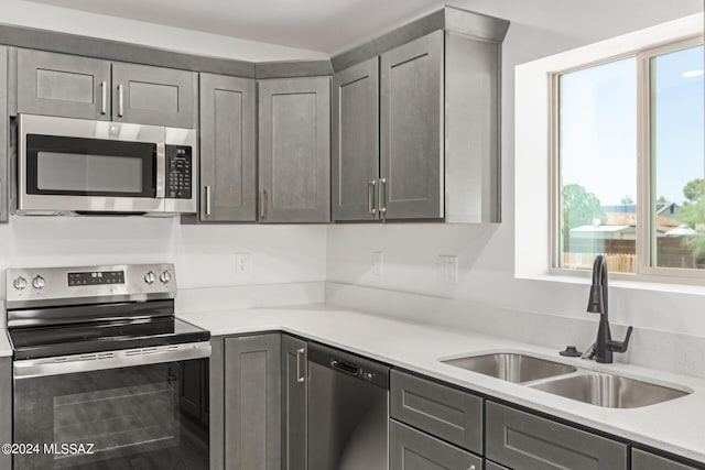 kitchen with light stone countertops, appliances with stainless steel finishes, sink, and gray cabinetry