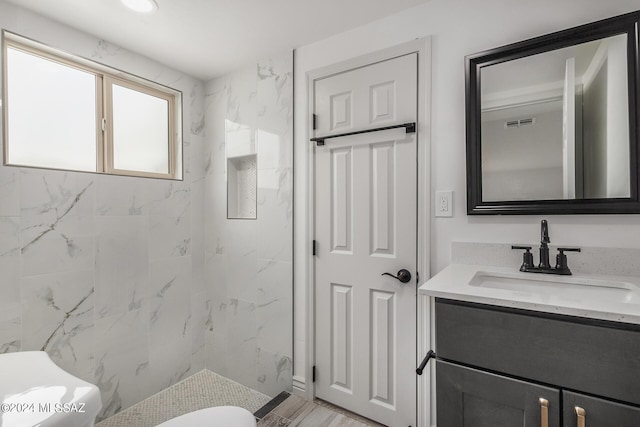 bathroom featuring toilet, vanity, and a tile shower