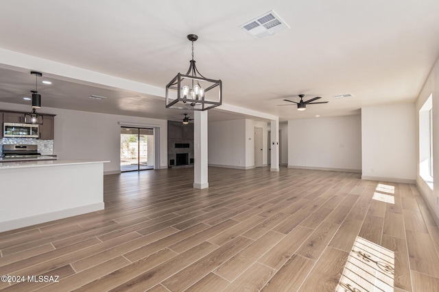 unfurnished living room with a fireplace, ceiling fan with notable chandelier, and wood-type flooring