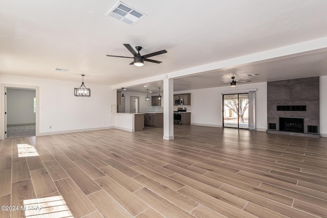 unfurnished living room with ceiling fan with notable chandelier and a fireplace