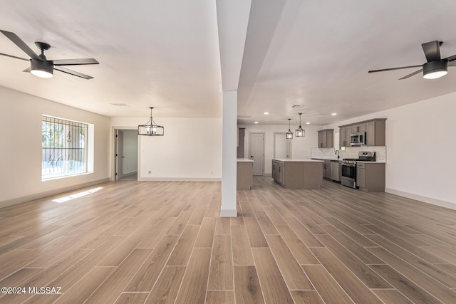 unfurnished living room with light wood-type flooring and ceiling fan with notable chandelier