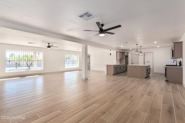 unfurnished living room featuring ceiling fan with notable chandelier, light hardwood / wood-style floors, and a healthy amount of sunlight