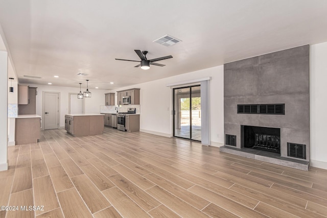 unfurnished living room with a large fireplace and ceiling fan with notable chandelier