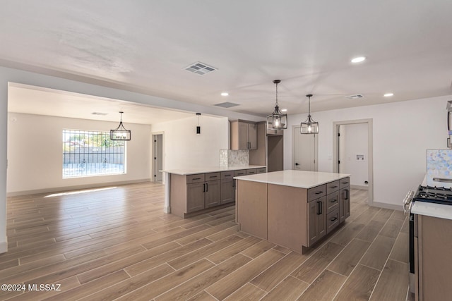 kitchen with hardwood / wood-style floors, a kitchen island, decorative backsplash, stainless steel range with gas cooktop, and hanging light fixtures