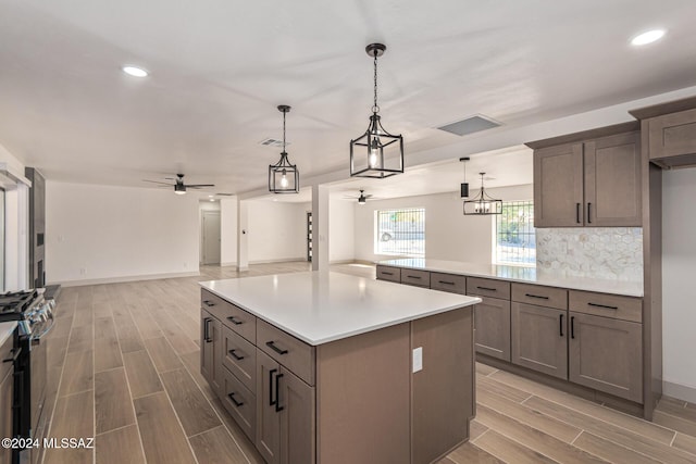 kitchen with stainless steel gas range oven, ceiling fan, backsplash, decorative light fixtures, and a center island