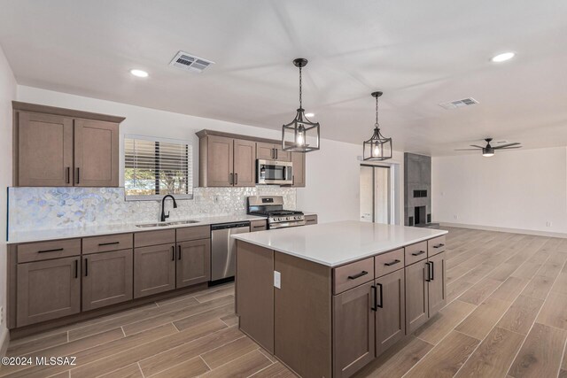 kitchen featuring appliances with stainless steel finishes, a center island, decorative light fixtures, sink, and ceiling fan