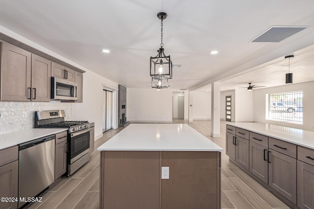 kitchen with a center island, stainless steel appliances, backsplash, hanging light fixtures, and ceiling fan