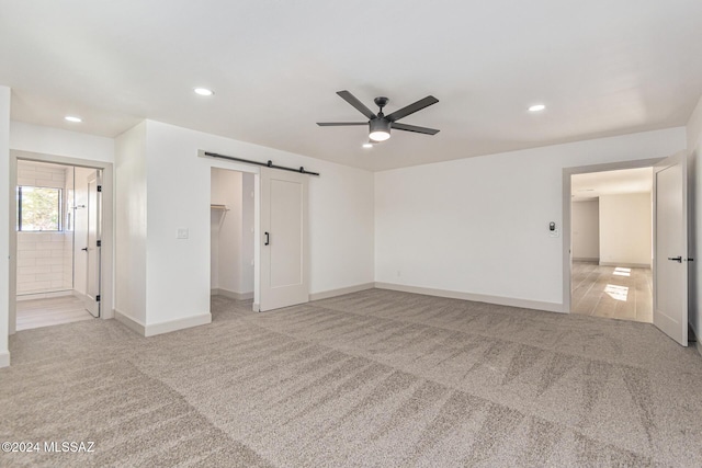 interior space with a walk in closet, light carpet, a closet, ceiling fan, and a barn door