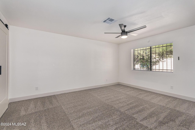 carpeted empty room featuring ceiling fan and a barn door