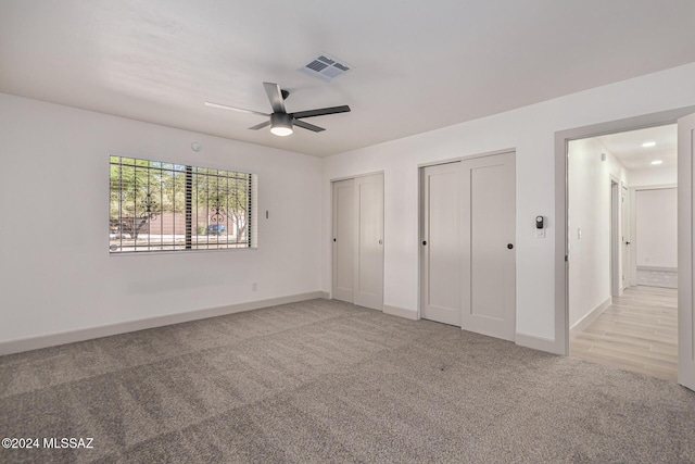 unfurnished bedroom featuring ceiling fan, light carpet, and multiple closets