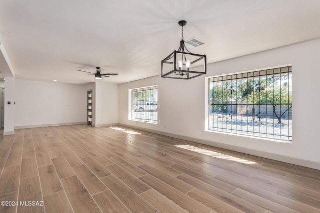 unfurnished living room with plenty of natural light, ceiling fan with notable chandelier, and hardwood / wood-style floors