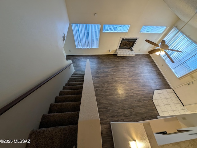 stairway featuring hardwood / wood-style flooring, ceiling fan, a tiled fireplace, and a high ceiling