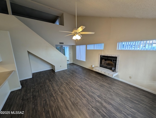 unfurnished living room featuring a tile fireplace, high vaulted ceiling, ceiling fan, dark wood-type flooring, and a textured ceiling