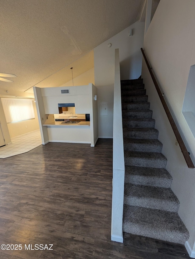 stairway featuring lofted ceiling, wood-type flooring, and a textured ceiling