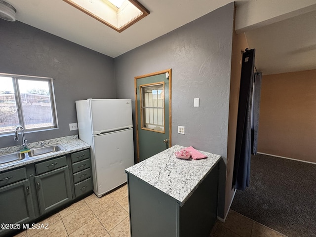 kitchen featuring sink, light colored carpet, white refrigerator, and vaulted ceiling with skylight