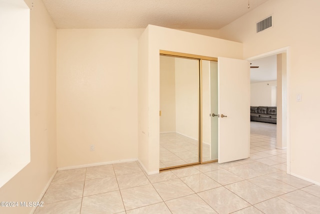 unfurnished bedroom featuring a textured ceiling, light tile patterned flooring, a closet, and vaulted ceiling