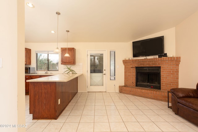 kitchen with sink, decorative light fixtures, light tile patterned floors, kitchen peninsula, and a brick fireplace