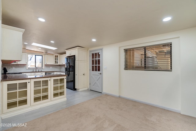 kitchen with white cabinetry, decorative backsplash, stove, light colored carpet, and black refrigerator with ice dispenser