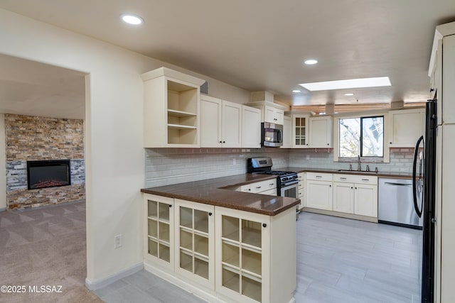 kitchen with sink, a skylight, appliances with stainless steel finishes, kitchen peninsula, and white cabinets