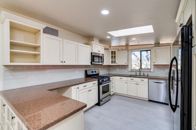 kitchen with a peninsula, a sink, dark countertops, a skylight, and appliances with stainless steel finishes