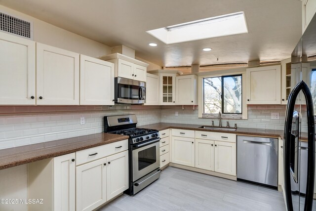 kitchen with a sink, a skylight, decorative backsplash, a peninsula, and appliances with stainless steel finishes
