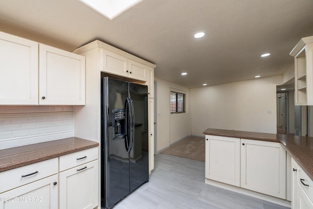 kitchen with white cabinetry, black fridge with ice dispenser, and kitchen peninsula