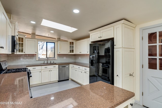 kitchen featuring sink, a skylight, stainless steel appliances, decorative backsplash, and white cabinets