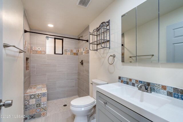 bathroom featuring a tile shower, toilet, vanity, and visible vents