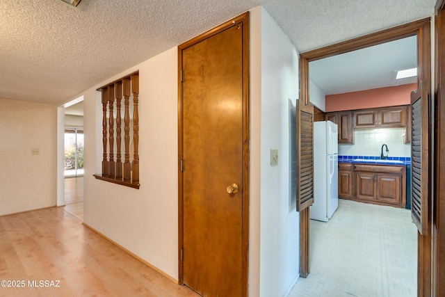 hall featuring sink, light wood-type flooring, and a textured ceiling