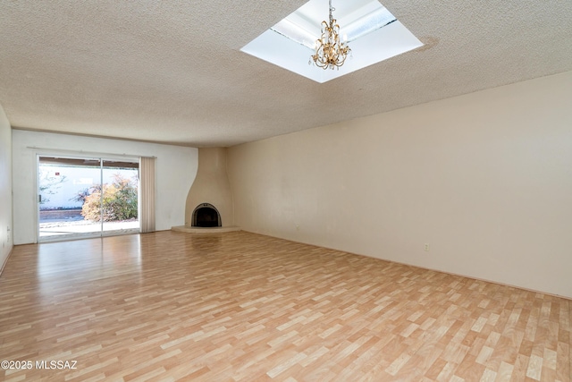 unfurnished living room with a textured ceiling, light hardwood / wood-style flooring, a notable chandelier, and a large fireplace