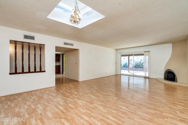 unfurnished living room featuring a textured ceiling, a fireplace, a skylight, light wood-type flooring, and an inviting chandelier