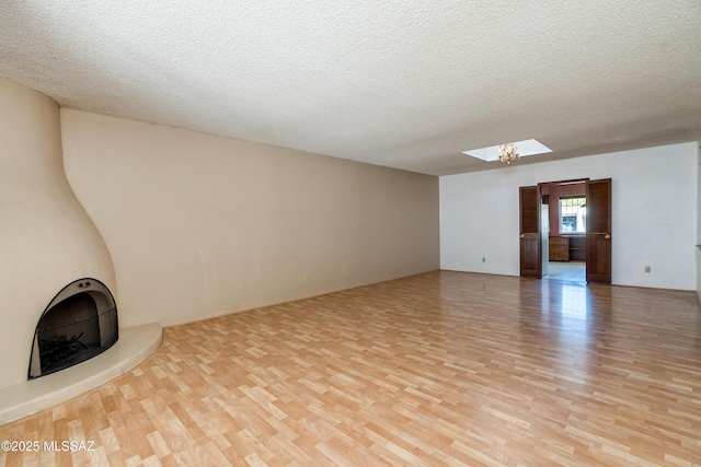 unfurnished living room with light hardwood / wood-style floors, a textured ceiling, and a skylight