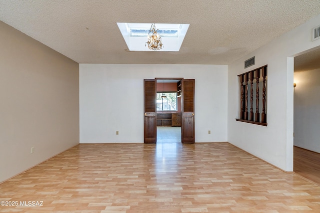 unfurnished living room with a textured ceiling, light hardwood / wood-style flooring, a skylight, and an inviting chandelier