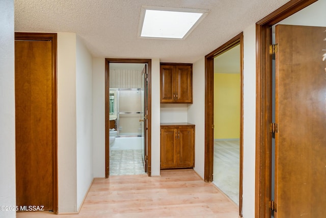 hall with light hardwood / wood-style floors, a textured ceiling, and a skylight