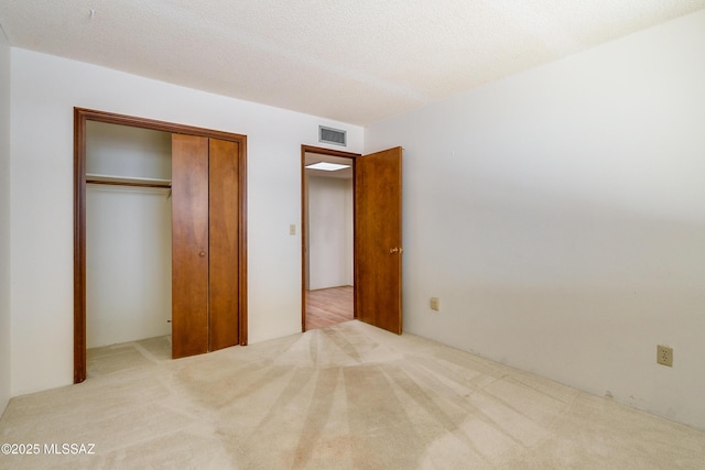 unfurnished bedroom featuring a textured ceiling, a closet, and light carpet