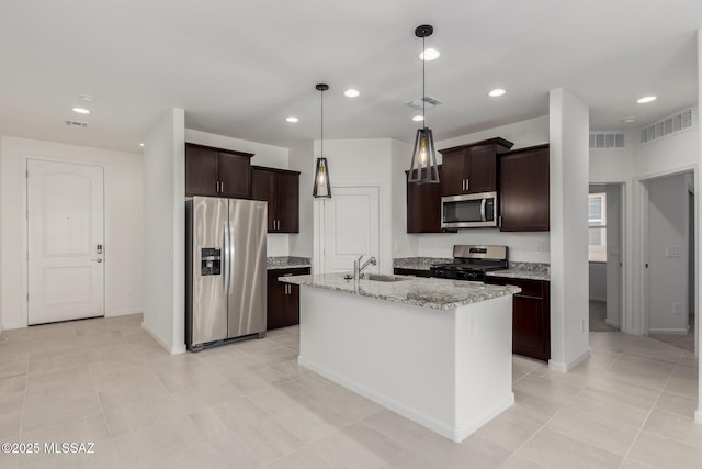 kitchen featuring light stone countertops, pendant lighting, appliances with stainless steel finishes, sink, and a kitchen island with sink