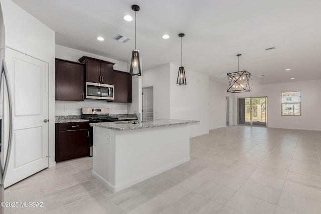 kitchen with pendant lighting, an island with sink, stainless steel appliances, dark brown cabinets, and light stone counters