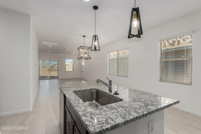 kitchen with an island with sink, decorative light fixtures, light stone countertops, and sink